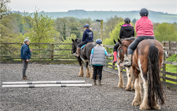 A group of riders and horses in an arena, with a coach and helper.